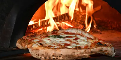 La cocina de La Fainá: una pizza saliendo del horno de leña